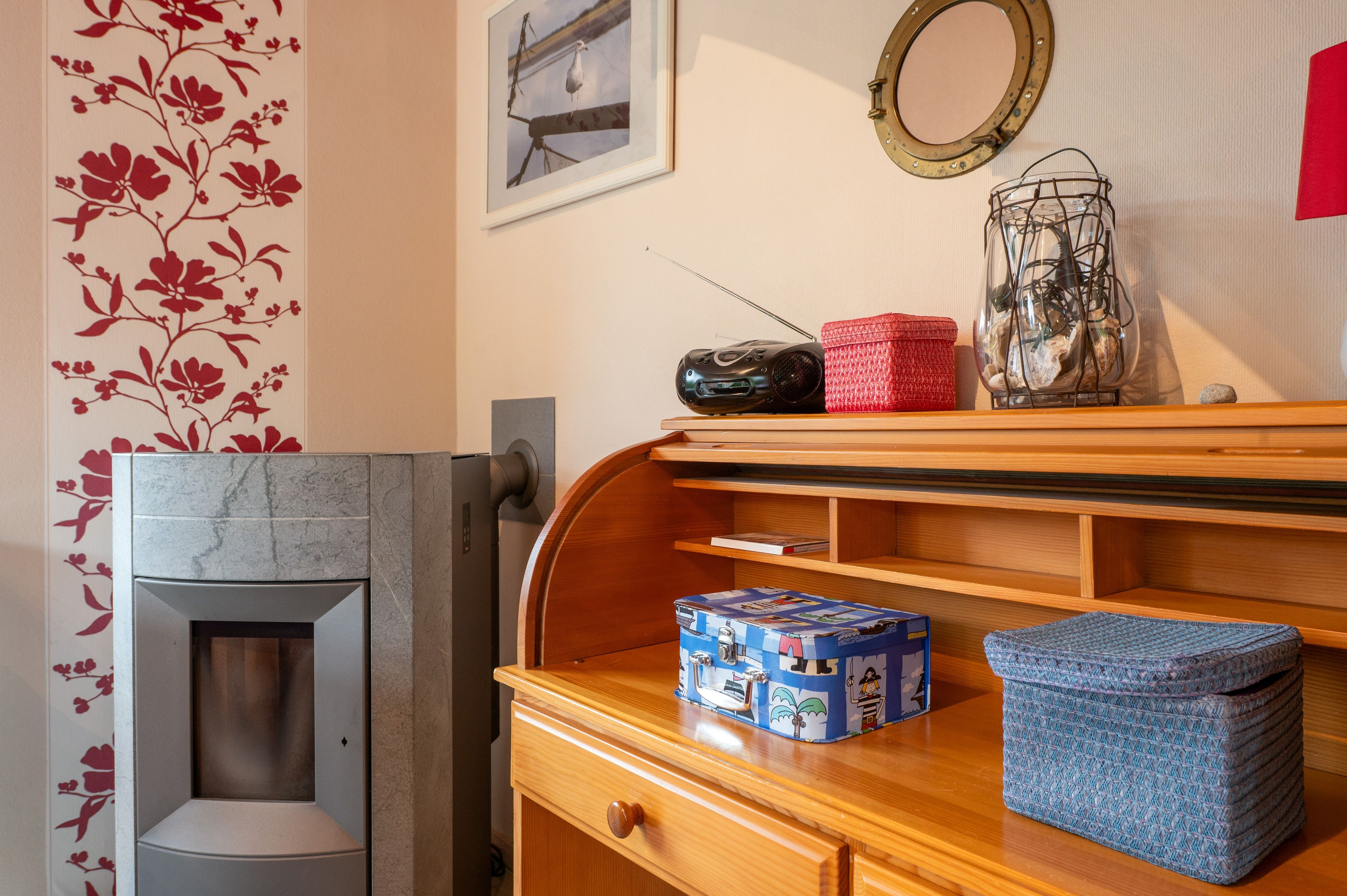 A room with a wooden dresser, a framed picture, a mirror, and a decorative wall with floral wallpaper.