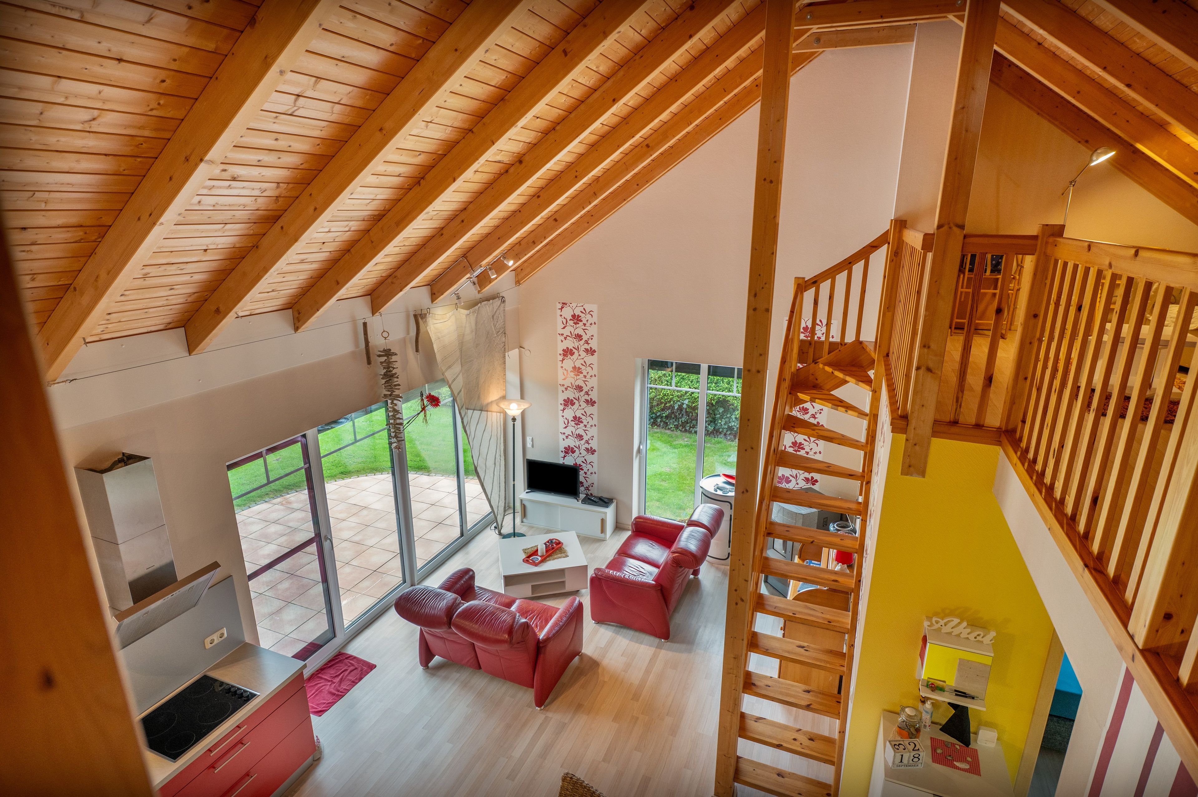 Un espacio habitable amplio con techo alto, un sofá rojo, un televisor y una escalera que lleva a un nivel superior.