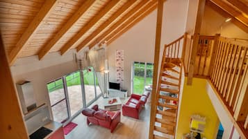 Un espacio habitable amplio con techo alto, un sofá rojo, un televisor y una escalera que lleva a un nivel superior.