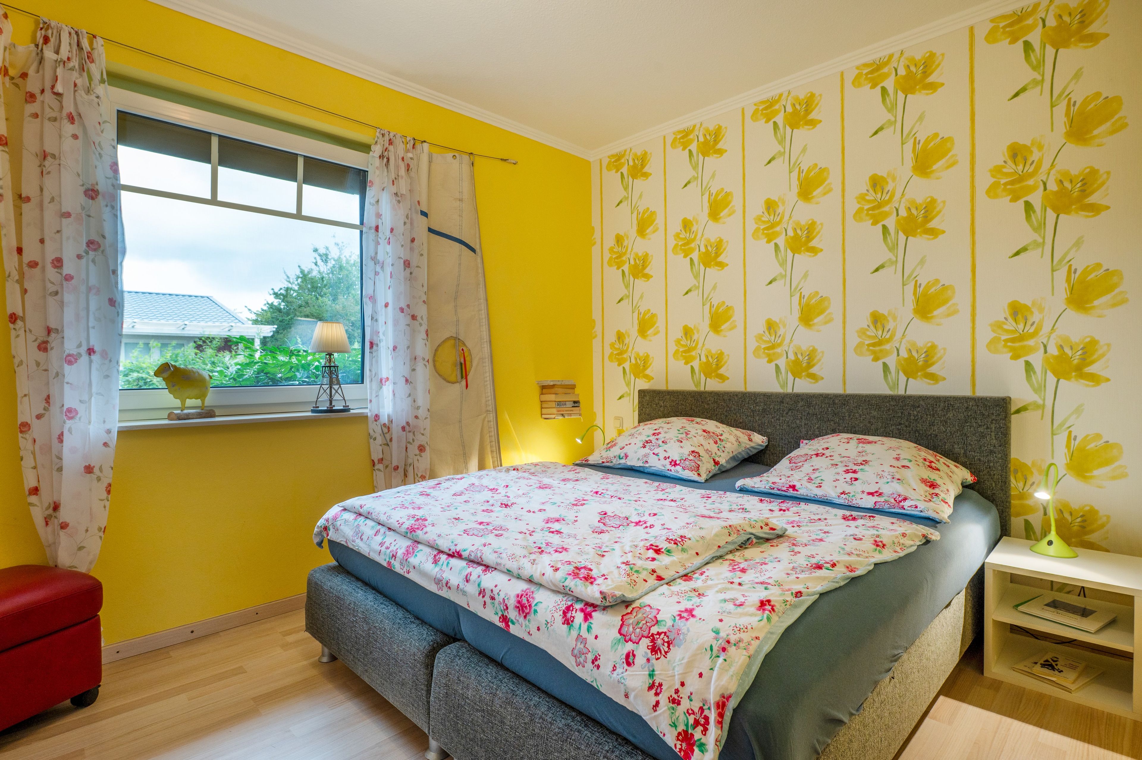 Une chambre à coucher avec un lit, une table de chevet, une lampe et une fenêtre avec des rideaux.