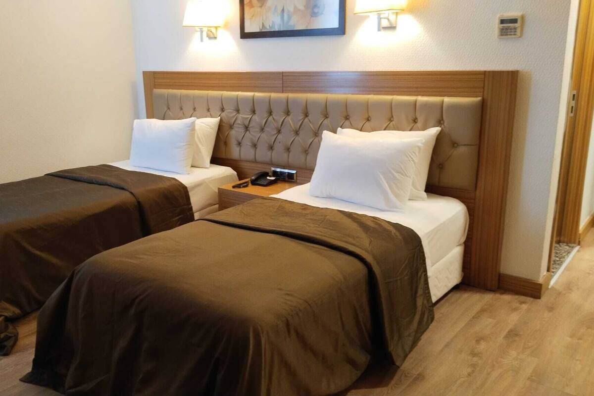 A hotel room with two beds, a bedside table with a phone, and a wall-mounted lamp.