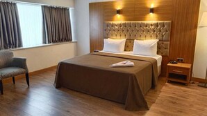 Een hotelkamer met een groot bed, een houten hoofdbord, een nachtkastje en een stoel.