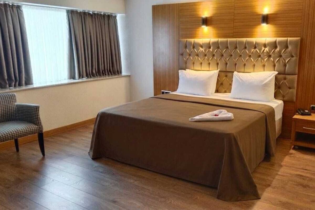 A hotel room with a large bed, a wooden headboard, a bedside table, and a chair.