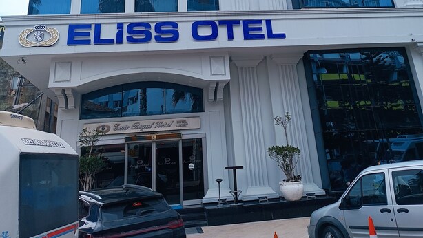 Een modern hotel met een glazen gevel die reflecteert, een opvallend 'ELISS OTEL' bord en een klassieke architectuur.