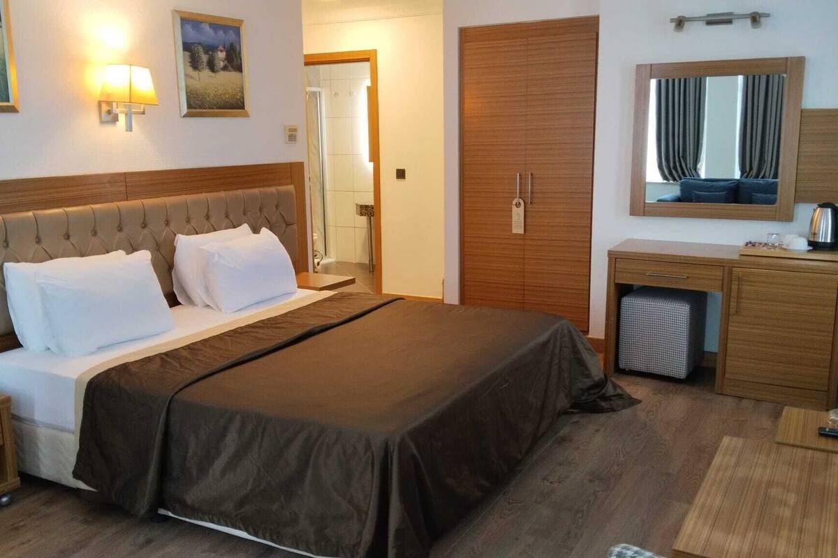 A hotel room with a bed, bedside tables, a desk, a mirror, and a wardrobe.