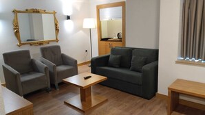Een woonkamer met twee fauteuils, een bank, een salontafel, een spiegel en een lamp.
