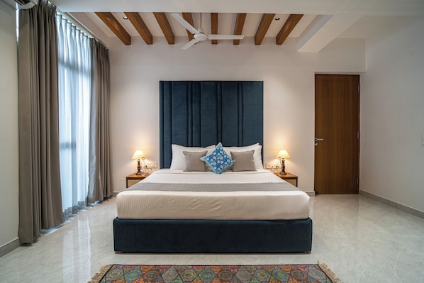 A bedroom with a bed, bedside lamps, a ceiling fan, a wooden door, and a patterned rug.