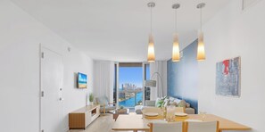 Ein modernes Wohnzimmer mit Essbereich, großen Fenstern und Blick auf die Stadt, sparsam eingerichtet.