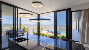 Una cocina moderna con una isla grande, un comedor con mesa, y vistas a una piscina y montañas.