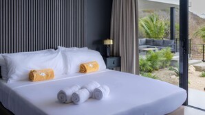 Habitación de hotel con una cama grande, dos almohadas, una mesita de noche, una lámpara y vistas al exterior.