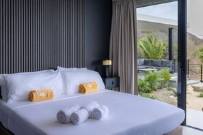 Ein Hotelzimmer mit einem großen Bett, zwei Kissen, einem Nachttisch, einer Lampe und Blick ins Freie.
