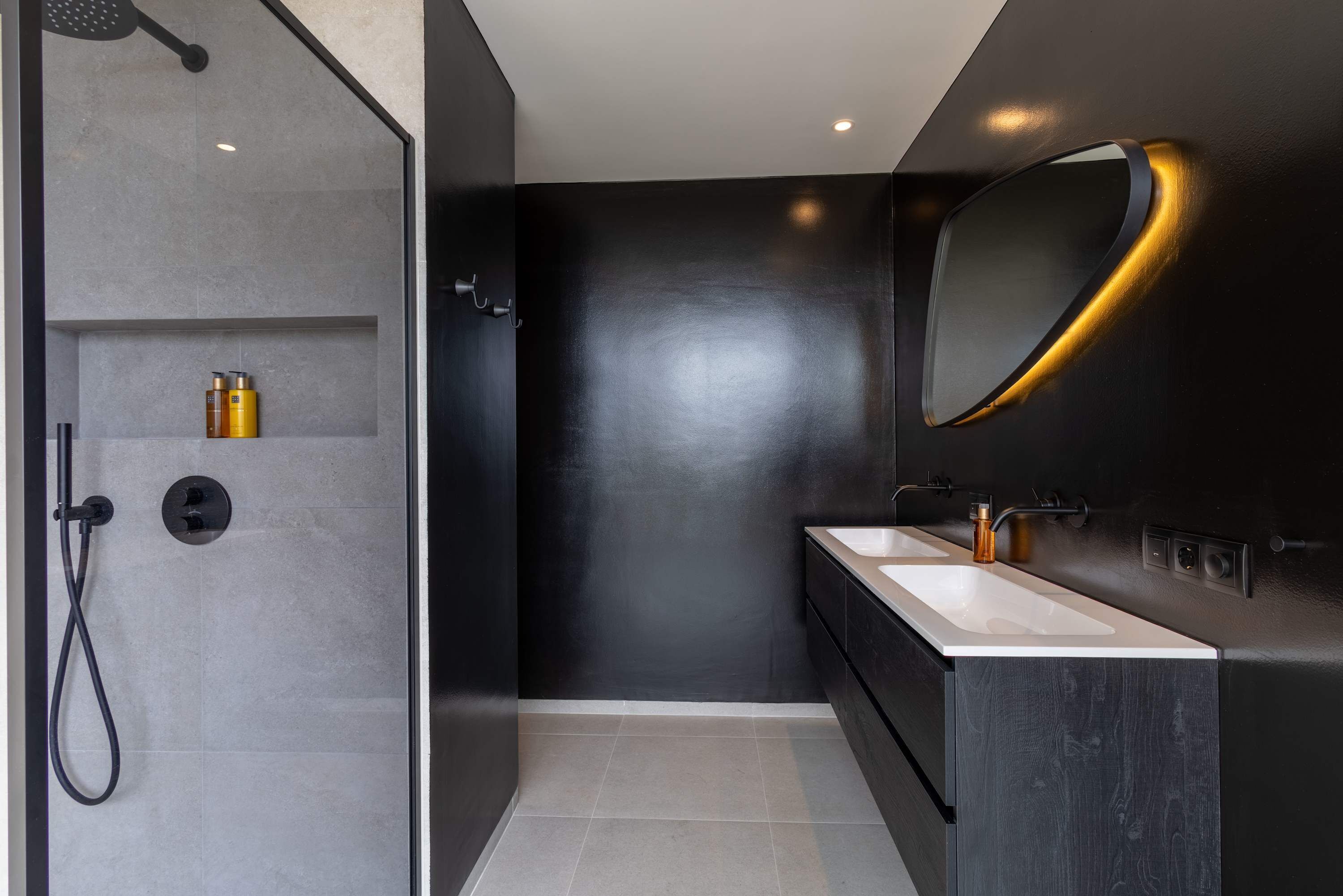 A modern bathroom with a glass-enclosed shower, two sinks, and a large mirror with a gold frame.