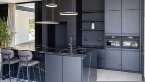 Una cocina moderna con una isla central, taburetes de bar, iluminación colgante y electrodomésticos integrados.