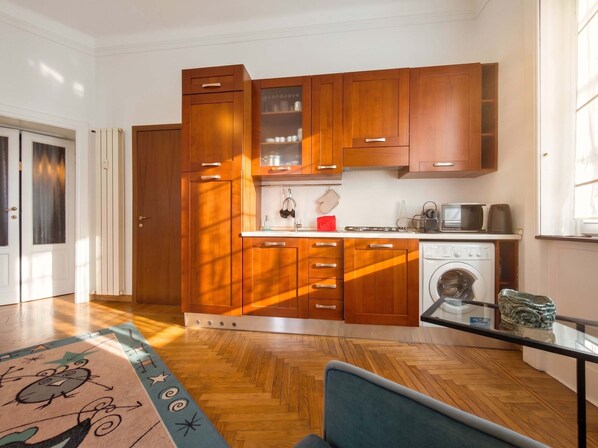 A compact kitchen with wooden cabinets, a built-in washing machine, and a glass coffee table. - Casa Nicole - Fine Stay in Navigli District (Milan)