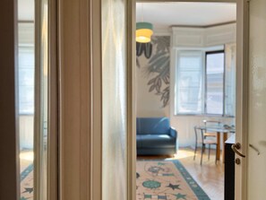 A doorway leading to a room with a patterned rug, a blue sofa, and a dining table. - Casa Nicole - Fine Stay in Navigli District (Milan)