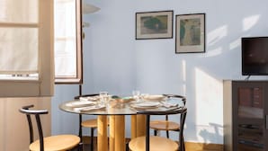 A dining area with a round glass table, four chairs, and a television on a cabinet. - Casa Nicole - Fine Stay in Navigli District (Milan)