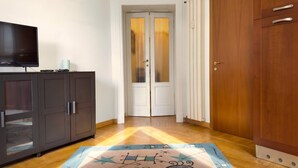 A hallway with a wooden floor, a television on a cabinet, and a door with frosted glass panels. - Casa Nicole - Fine Stay in Navigli District (Milan)