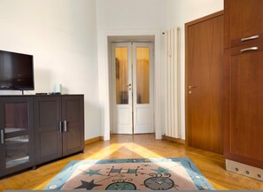 A hallway with a wooden floor, a television on a cabinet, and a door with frosted glass panels. - Casa Nicole - Fine Stay in Navigli District (Milan)