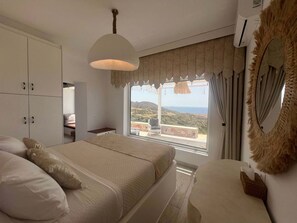 A bedroom with a bed, a wardrobe, a desk, and a large window with a view of the landscape. - Mythos Villa - Karpathos Secluded Panoramic Views (Karpathos)