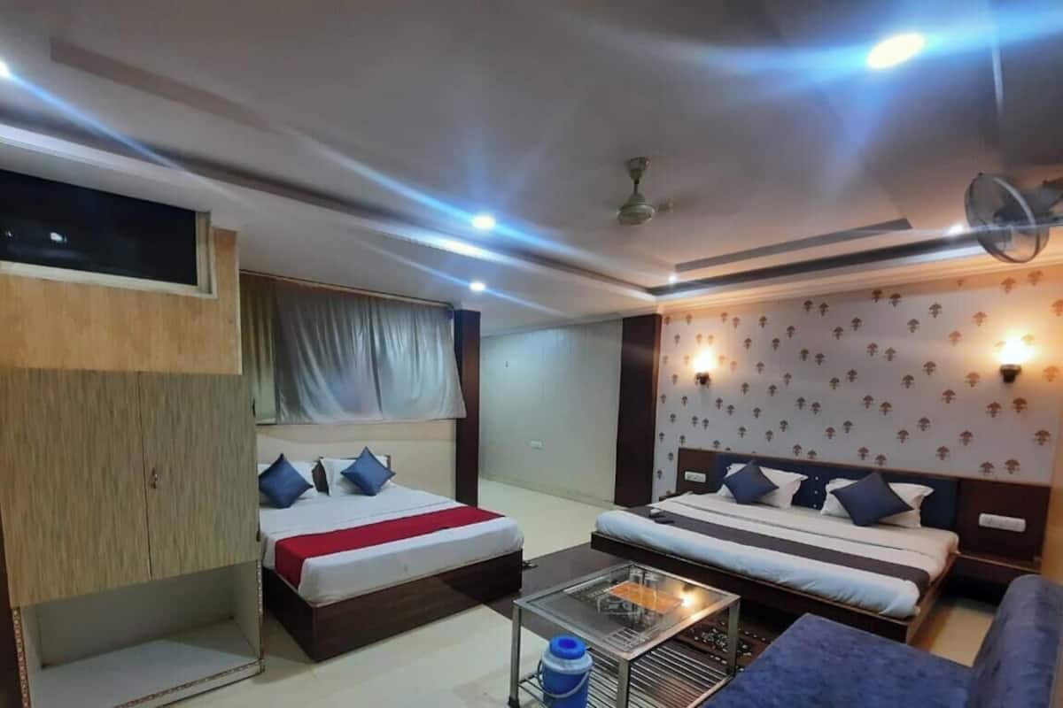Habitación de hotel con dos camas, televisión, ventilador de techo y una mesita con una botella de agua.
