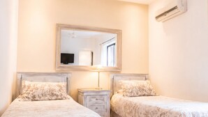 A bedroom with two beds, a ceiling fan, an air conditioning unit, and a mirror above the beds.