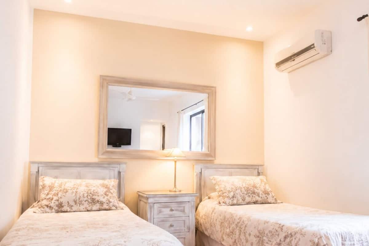 Un dormitorio con dos camas, un ventilador de techo, un equipo de aire acondicionado y un espejo sobre las camas.