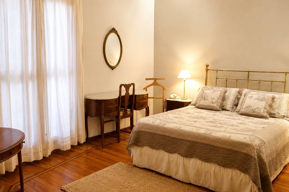 Un dormitorio con cama, mesita de noche, lámpara, silla y una pequeña mesa con bandeja.