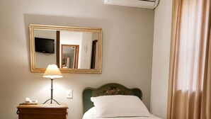 A hotel room with a bed, a nightstand with a lamp, a mirror, and a television.