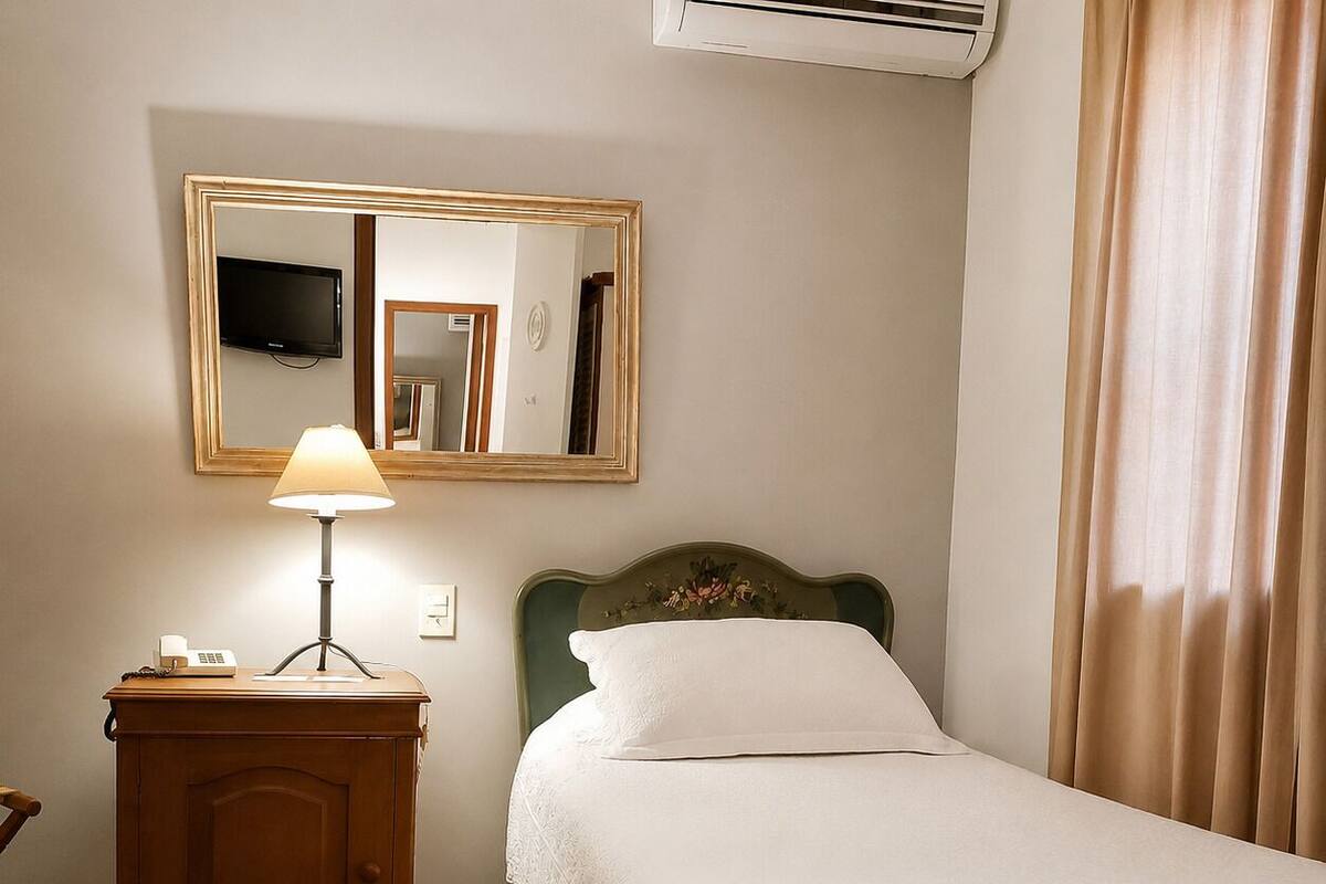 Una habitación de hotel con una cama, una mesita de noche con lámpara, un espejo y un televisor.