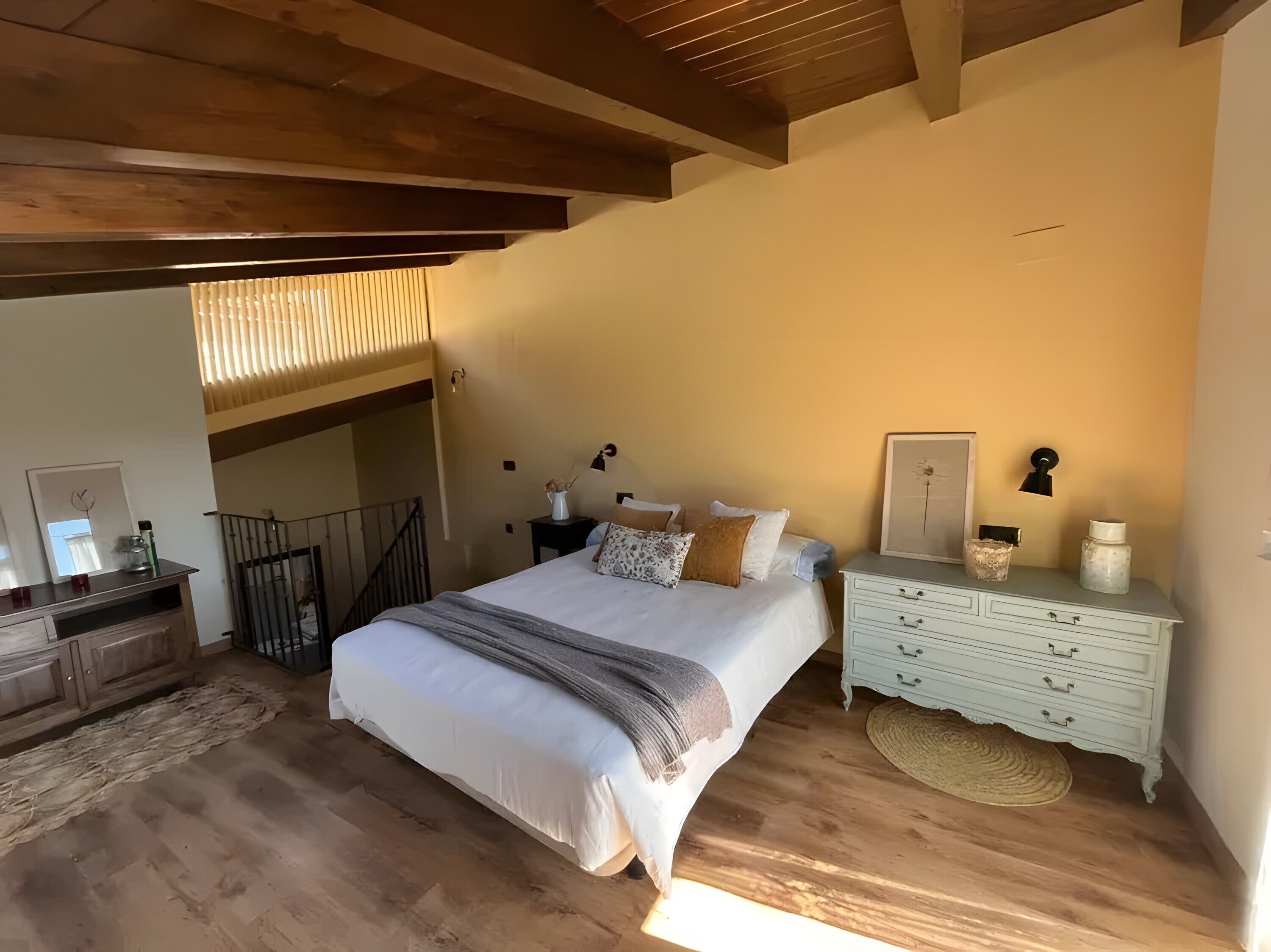 Un dormitorio con cama, mesitas de noche, cómoda, espejo y una escalera.