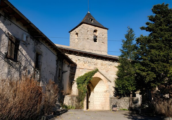 A stone tower with a bell, an arched passageway, and a building with a tiled roof.