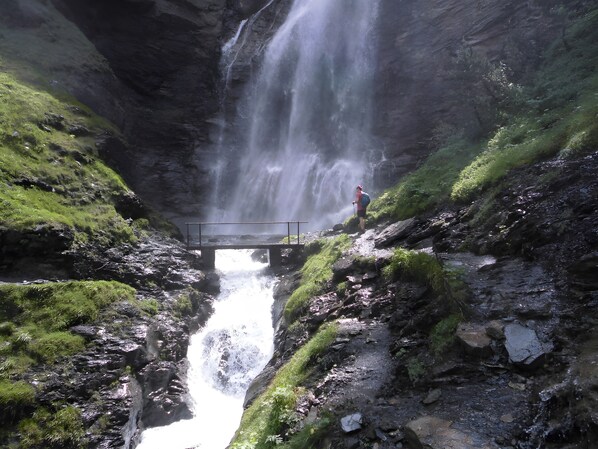 A waterfall with a bridge, rocky terrain, and greenery.