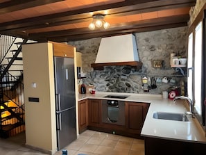 Uma cozinha com máquina de lavar louça embutida, geladeira de aço inoxidável, parede de pedra e escada de madeira.