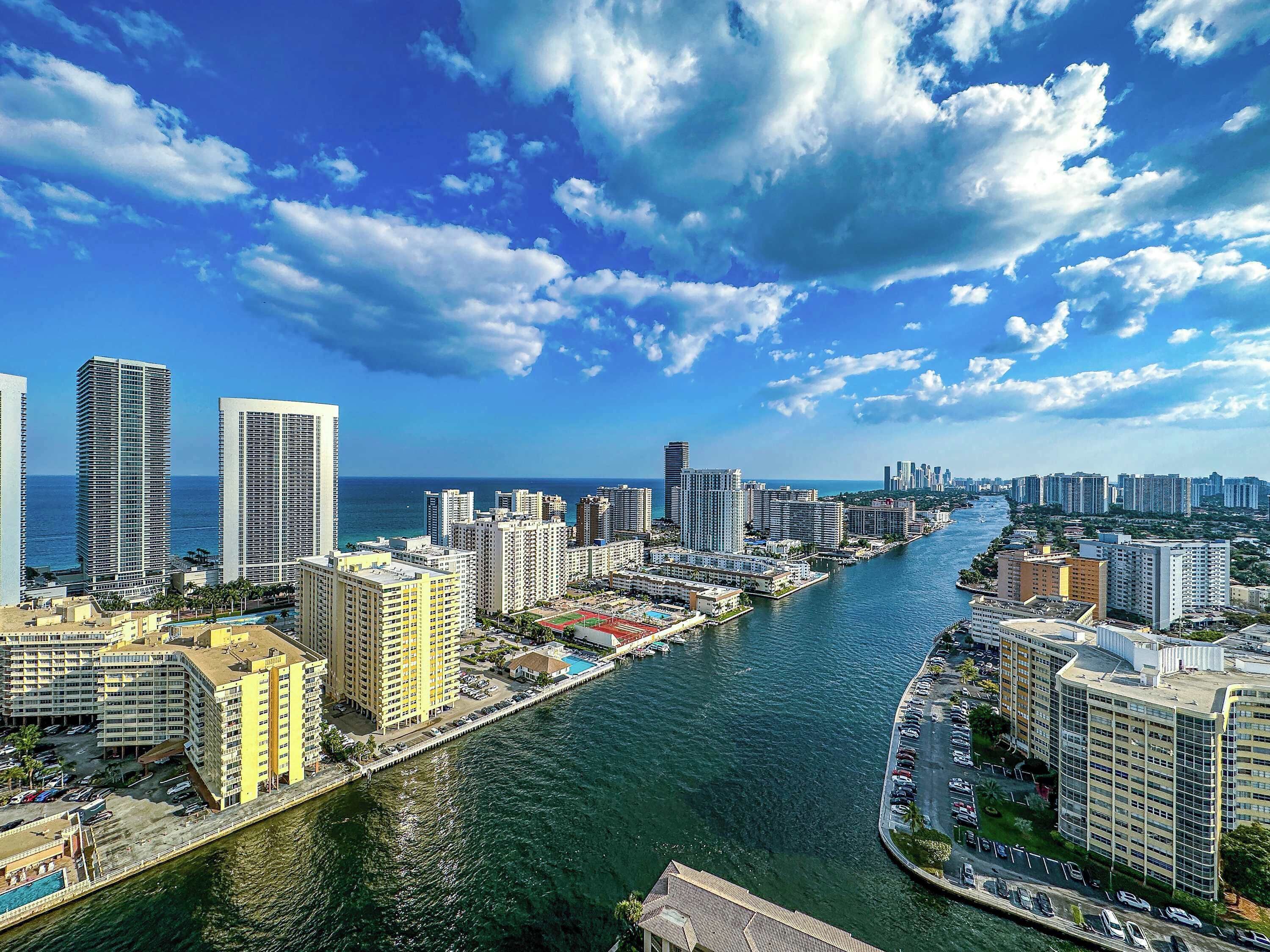 Un paisaje urbano costero con edificios altos, un puerto deportivo y cielo despejado.