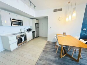 A modern kitchen with white cabinetry, stainless steel appliances, and a wooden dining table with chairs. - Top-Floor Intracoastal · 2BR Beachwalk Resort (Hallandale Beach)