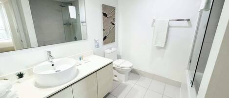 Une salle de bain moderne avec un grand miroir, un lavabo, des toilettes et un espace douche.