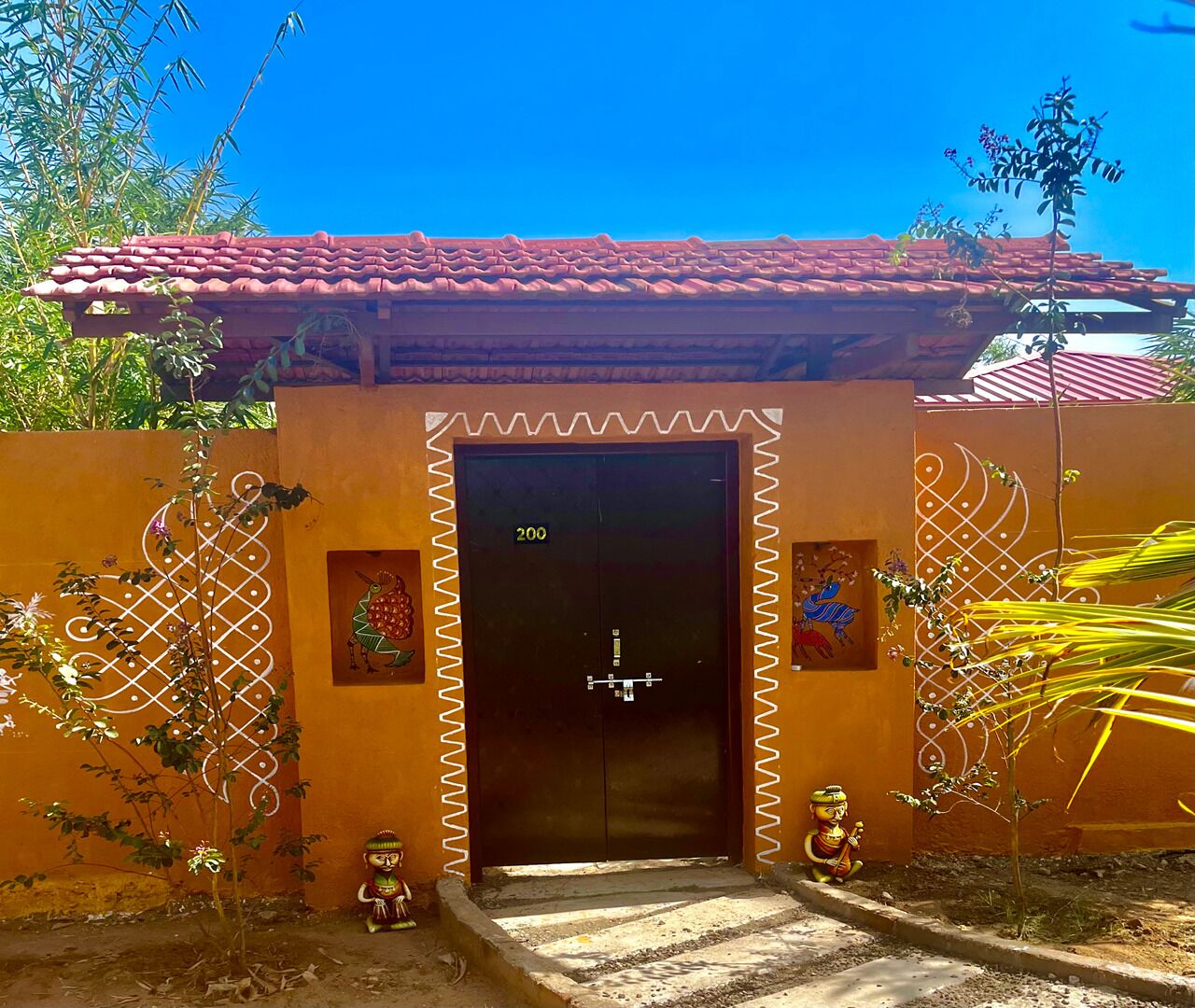Un edificio con techo de tejas rojas, una puerta negra marcada con el número 200 y decoración art ística en la pared.