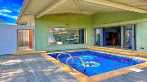 Una piscina con solárium azulejado, un porche cubierto y vistas del interior a través de un ventanal.