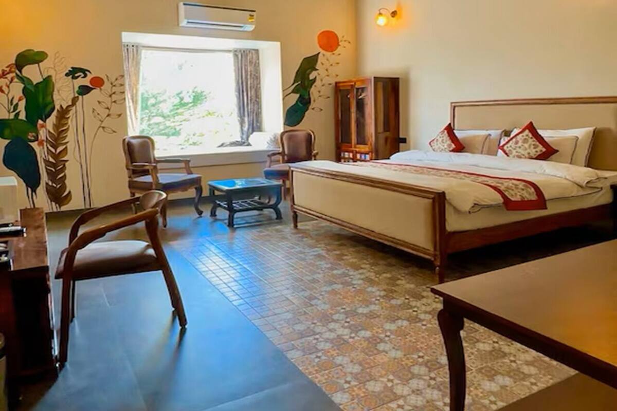 Habitación de hotel con cama, escritorio, silla, una mesita y ventana con cortinas.