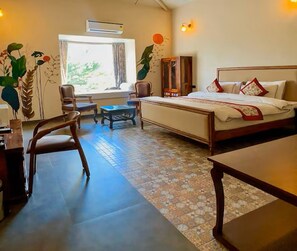 A hotel room with a bed, a desk, a chair, a small table, and a window with curtains.