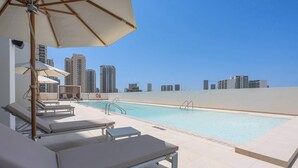 Ein Pool auf dem Dach mit Liegestühlen und Sonnenschirmen, umgeben von Hochhäusern.