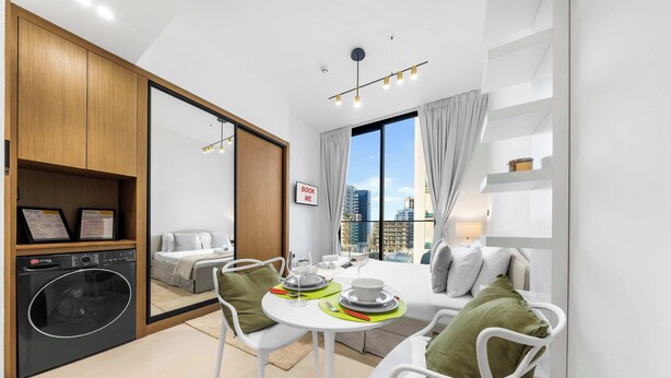 Eine moderne Küche mit integriertem Waschmaschinenanschluss, eine Essecke mit Tisch für zwei Personen und ein großes Fenster mit Blick auf die Stadt.