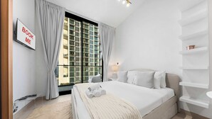 Ein modernes Hotelzimmer mit einem großen Bett, einem Fernseher, einem Fenster mit Vorhängen und Blick auf ein Gebäude.