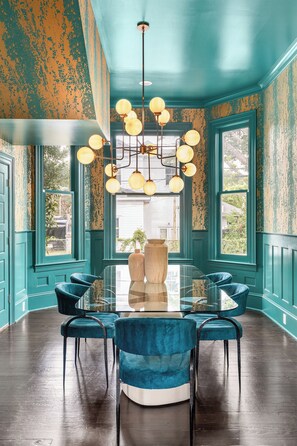 A dining room with a glass table surrounded by blue chairs, teal walls, and a chandelier with multiple light fixtures. - Maison Barnard | Starland's Most Stunning Home + Private Pool, Event Space (Savannah)