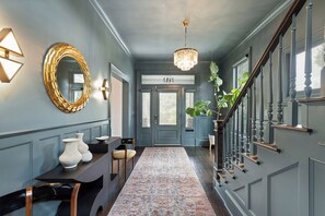 A hallway with a chandelier, a round mirror, a door labeled 'SOAS,' and a staircase with a railing. - Maison Barnard | Starland's Most Stunning Home + Private Pool, Event Space (Savannah)