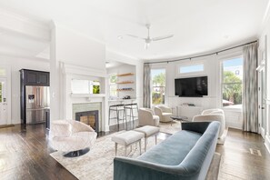 A spacious living room with a large sofa, a television, and a fireplace. - Maison Barnard | Starland's Most Stunning Home + Private Pool, Event Space (Savannah)