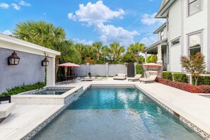 A swimming pool with a tiled edge, surrounded by a patio with outdoor furniture and umbrellas. - Maison Barnard | Starland's Most Stunning Home + Private Pool, Event Space (Savannah)