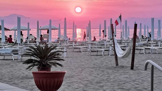 A beach with lounge chairs and umbrellas, a flag, and a sunset. - Apartment 8 with Sea View, Wi-Fi and Air Conditioning (Paestum)