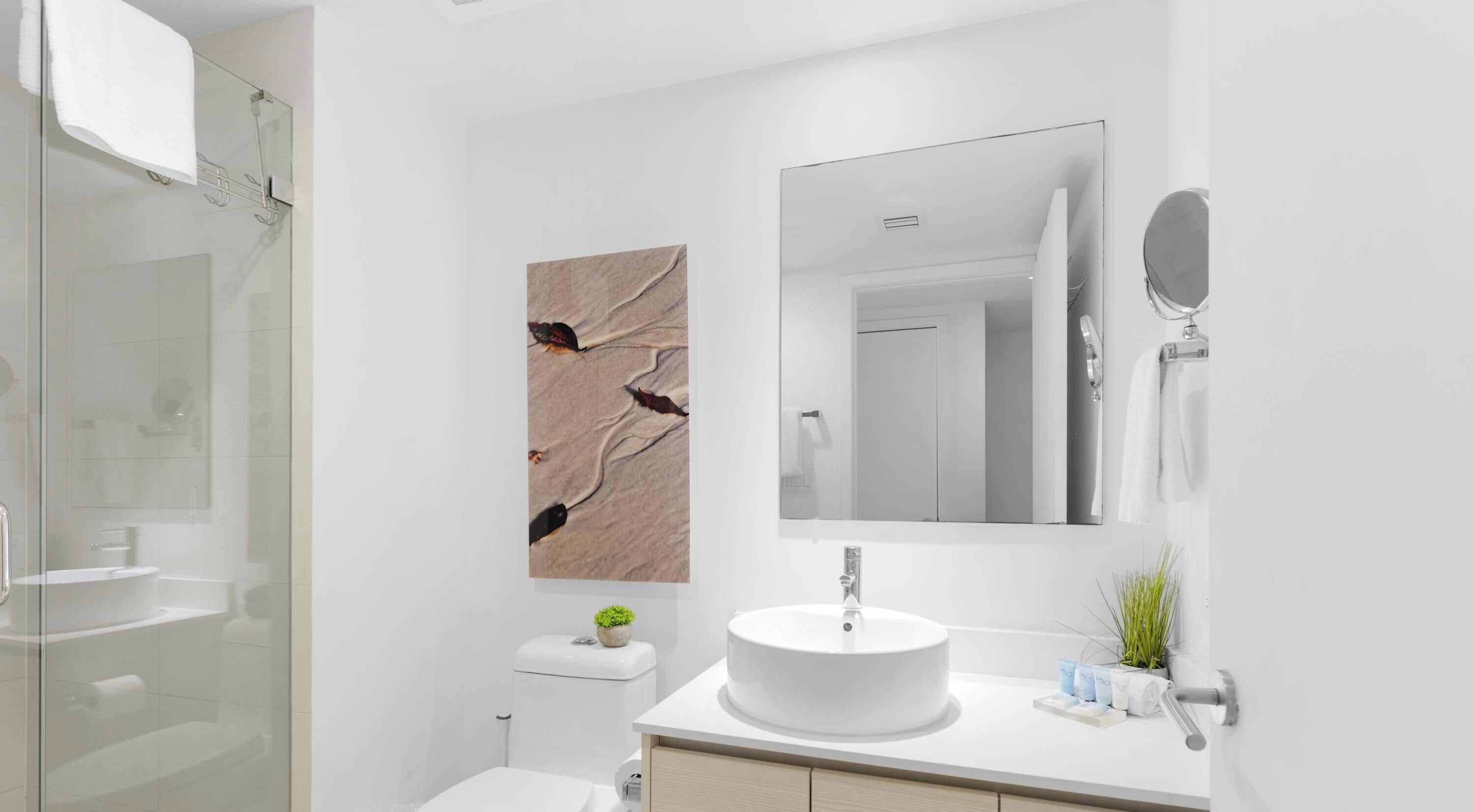 Un baño moderno con cabina de ducha de vidrio, lavamanos blanco y un espejo grande.