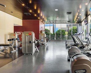 Ein Fitnessraum mit Cardiogeräten, Gewichten und großen Fenstern mit Blick ins Freie.